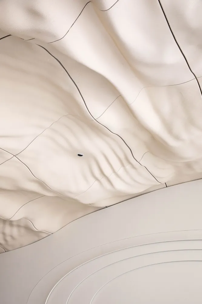 A modern interior space with a white ceiling featuring a wave-like pattern made of fabric, creating a contemporary atmosphere
