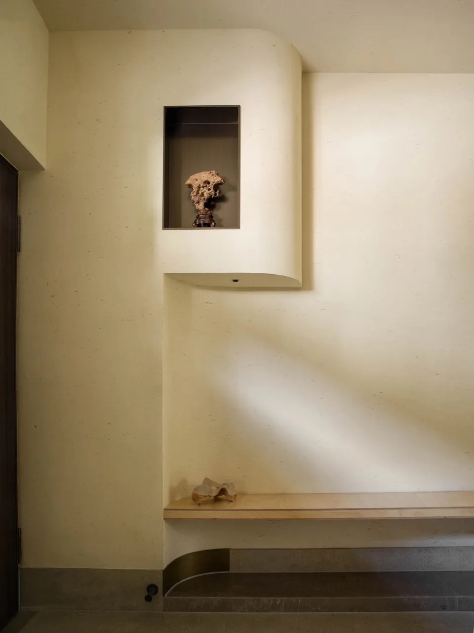 A solemn interior space with a bench against a wall featuring a small alcove with a skull, adding a unique decorative touch