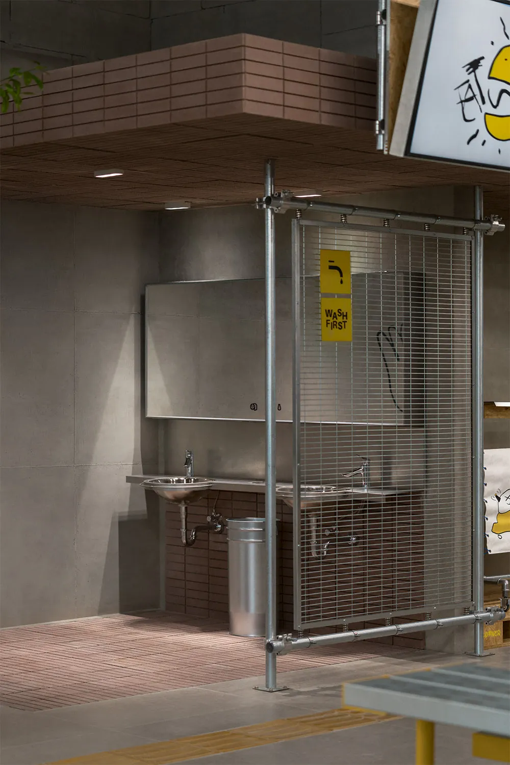 Industrial bathroom with metal fencing, two sinks, and a trash can, giving off a utilitarian and functional vibe