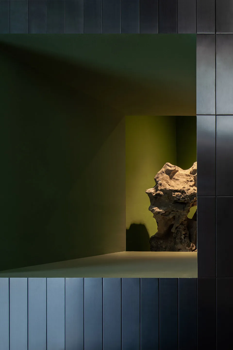 A serene interior space with a green wall and a stone countertop featuring two large rocks, creating a calm atmosphere
