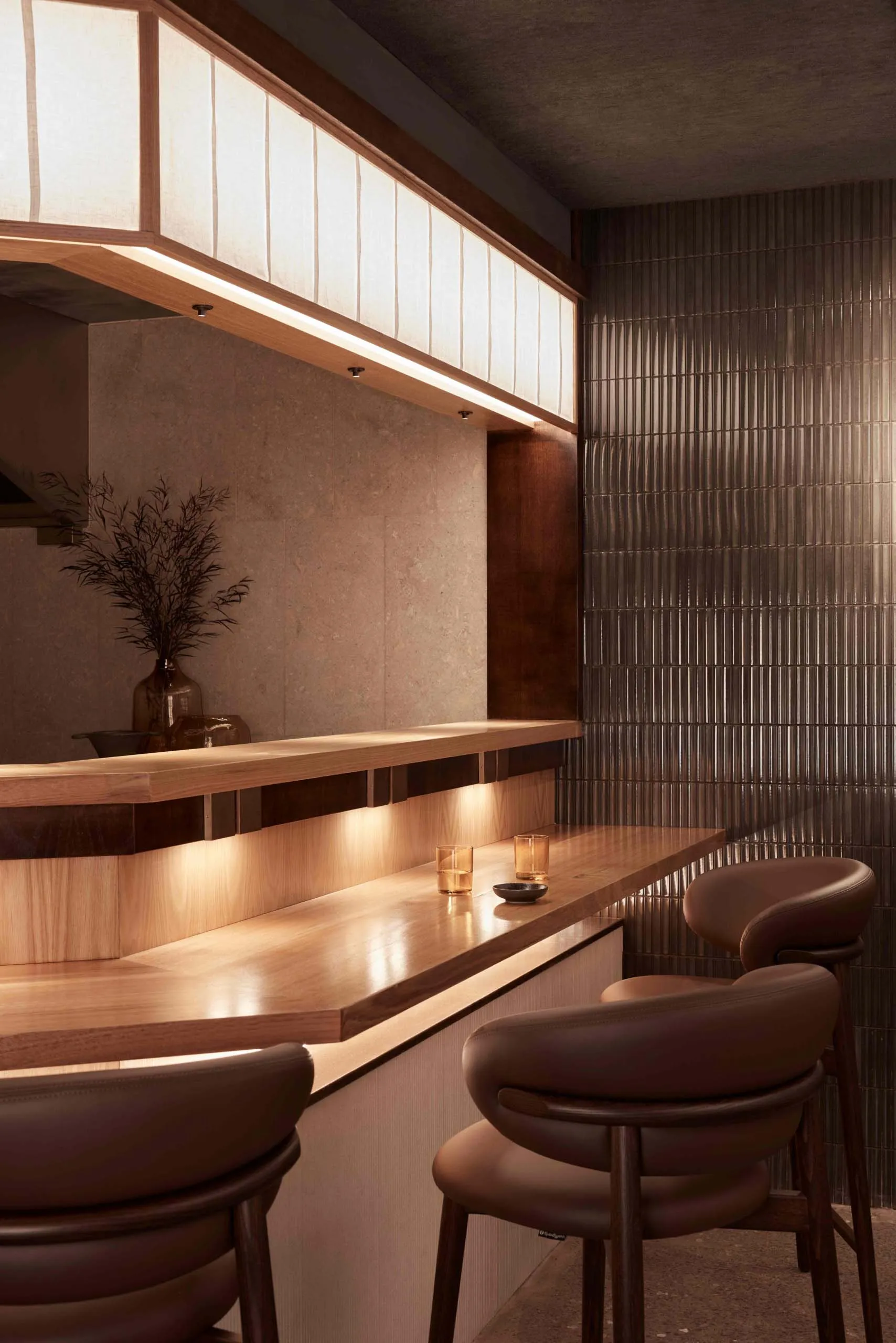 Warm and inviting bar area with a wooden countertop, brown leather chair, and decorative vases and cups