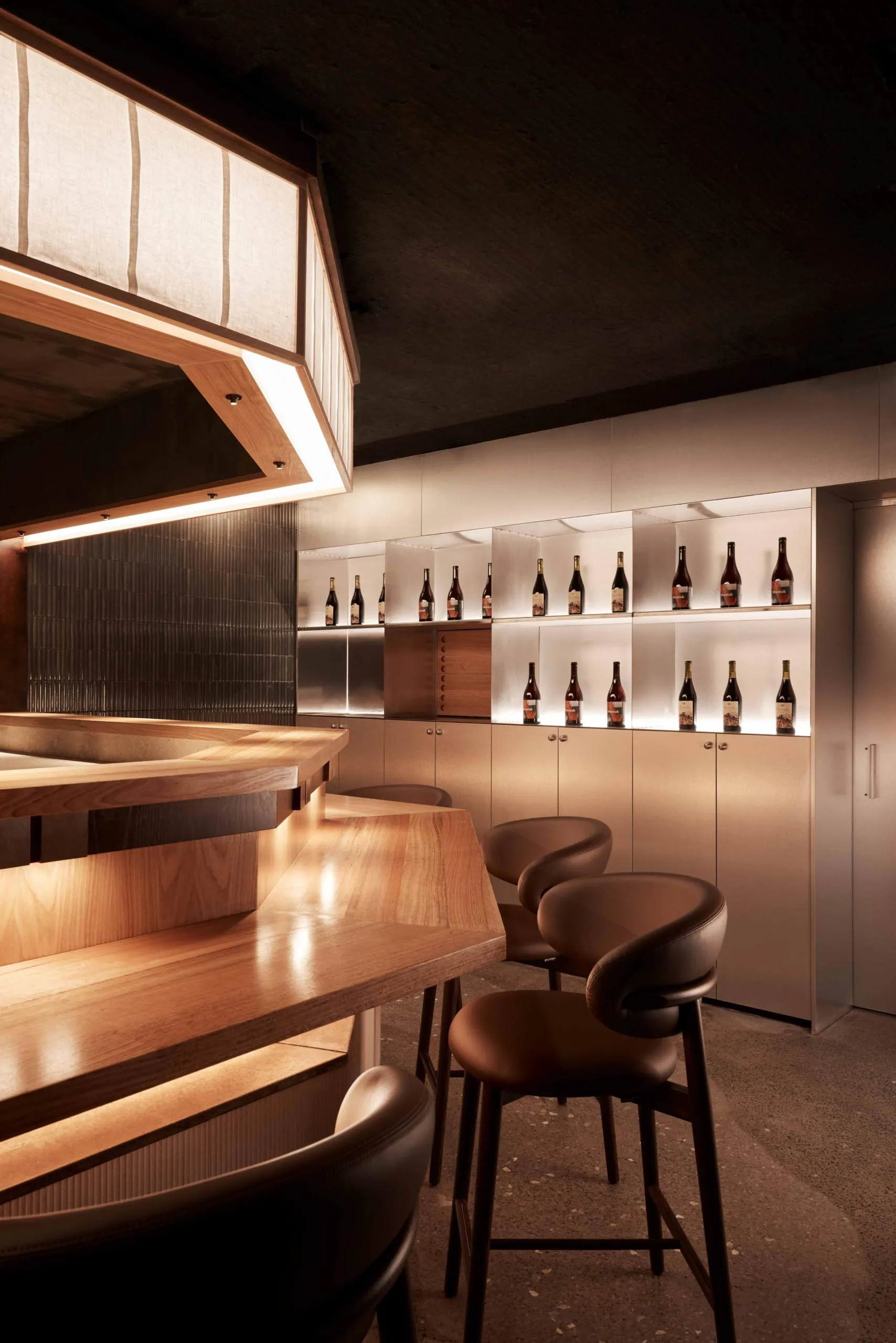 A bar area in a restaurant with a wooden countertop, wine bottles, and comfortable seating for patrons, creating a warm and inviting atmosphere