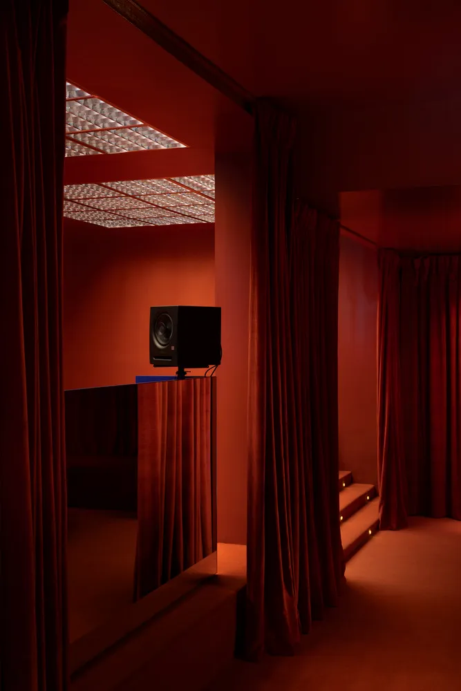 Cozy living space with orange walls, red curtains, a couch, two chairs, and two speakers for a relaxing atmosphere