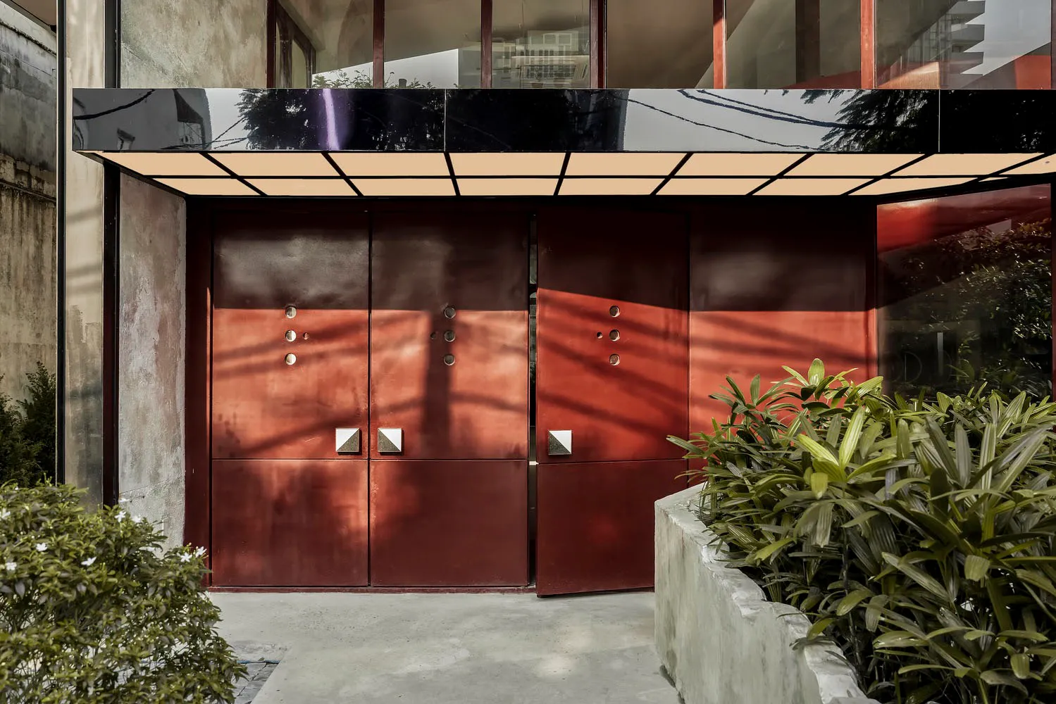 A modern entrance with two red doors that lead into a residential hallway, surrounded by potted plants
