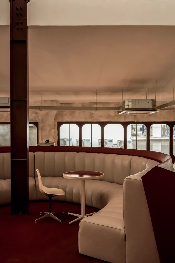 Modern living space with a circular seating arrangement, white couches, chairs, and a dining table, surrounded by red accent walls and natural light from windows
