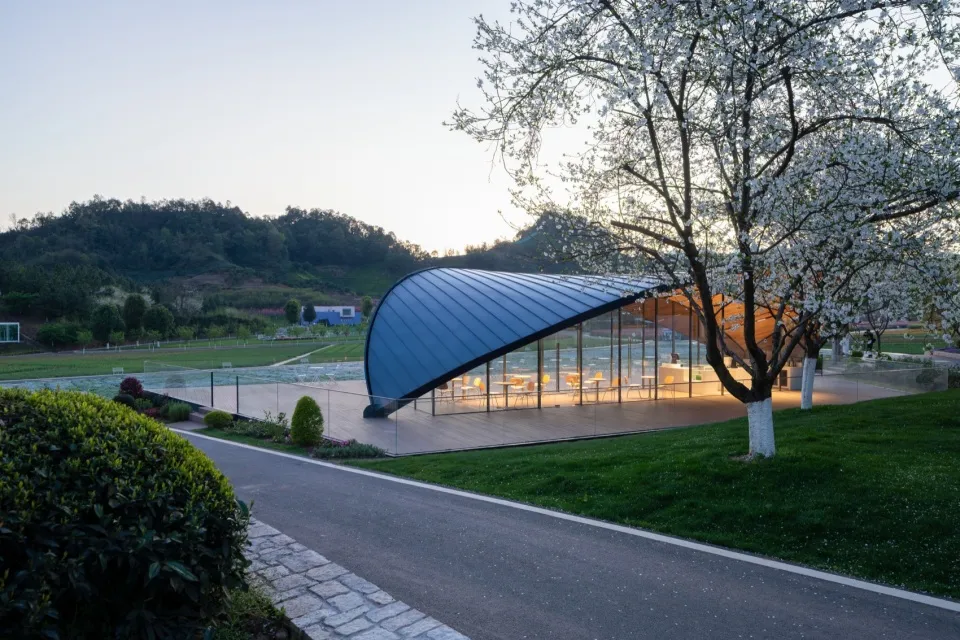 Bright and inviting open air space with a large glass wall, concrete or similar materials, and several chairs