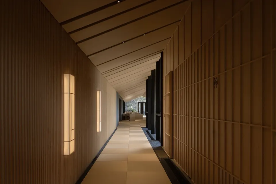 Empty hallway with wooden walls and flooring, lit by two lights on either side