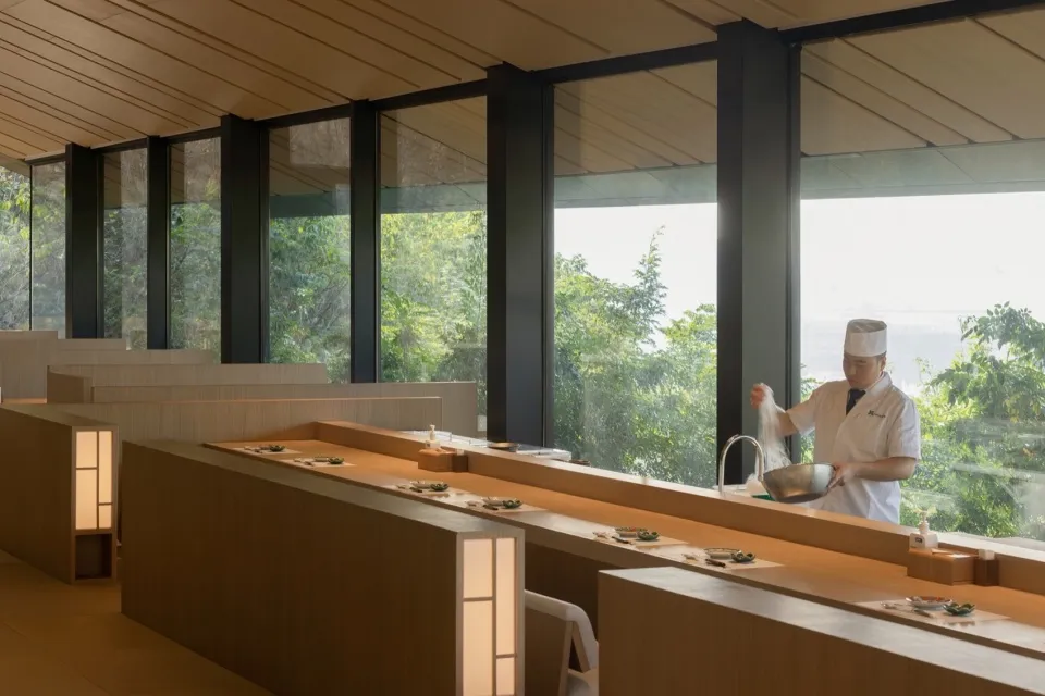 A bustling restaurant kitchen with a large window, sink, dining table, chairs, and people preparing food