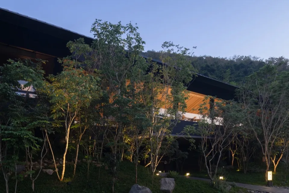 A modern building with a black exterior is surrounded by green trees, with a bench nearby, conveying a sense of tranquility and harmony between nature and architecture