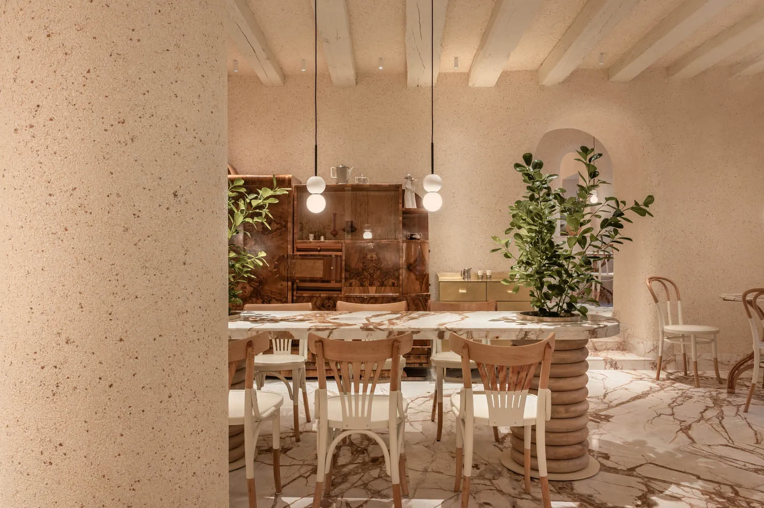 A modern kitchen with a dining table, wooden cabinets, and countertops, surrounded by potted plants and featuring ample storage and workspace