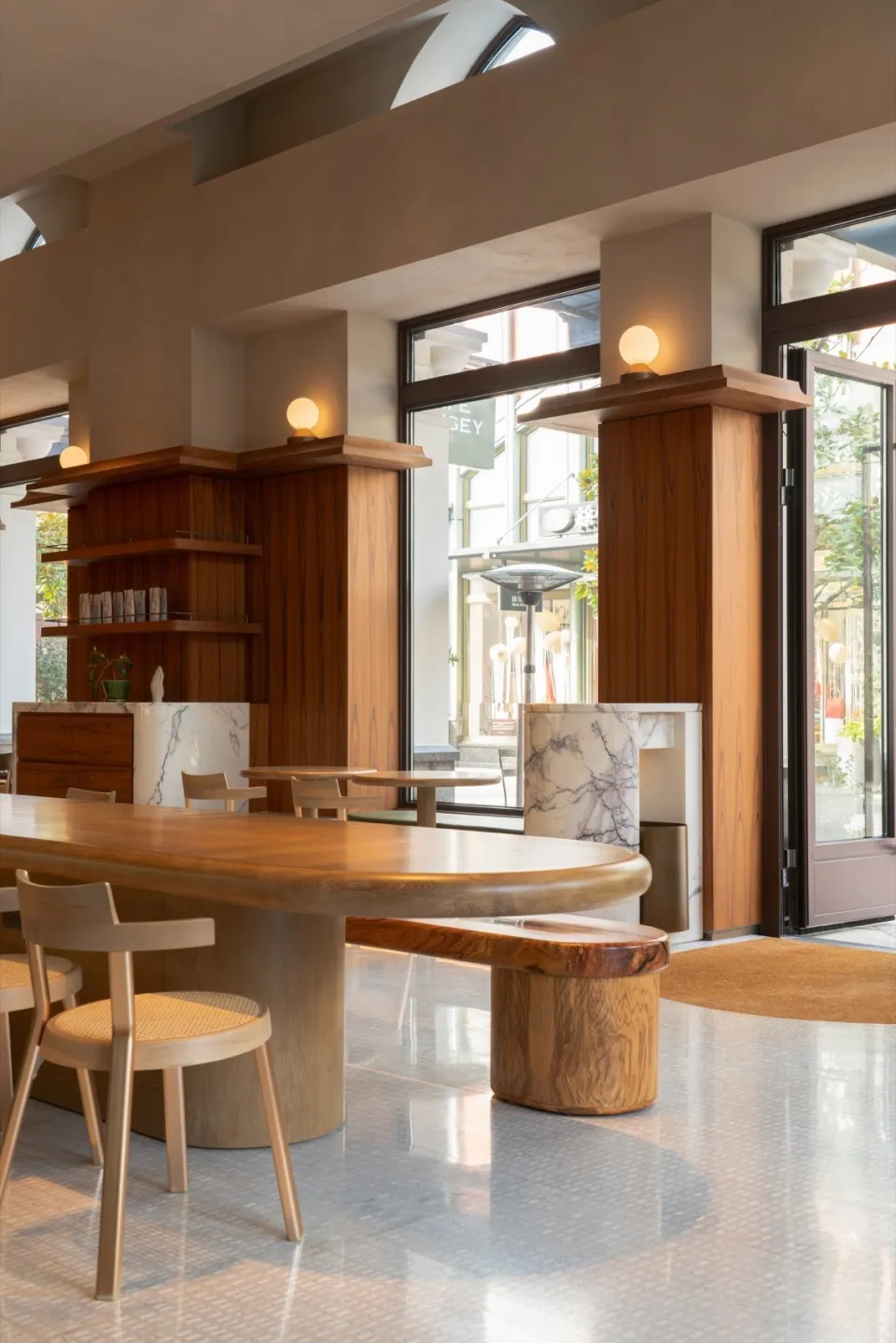 Well-lit restaurant interior with wooden tables, marble countertops, and a large window allowing natural light to enter