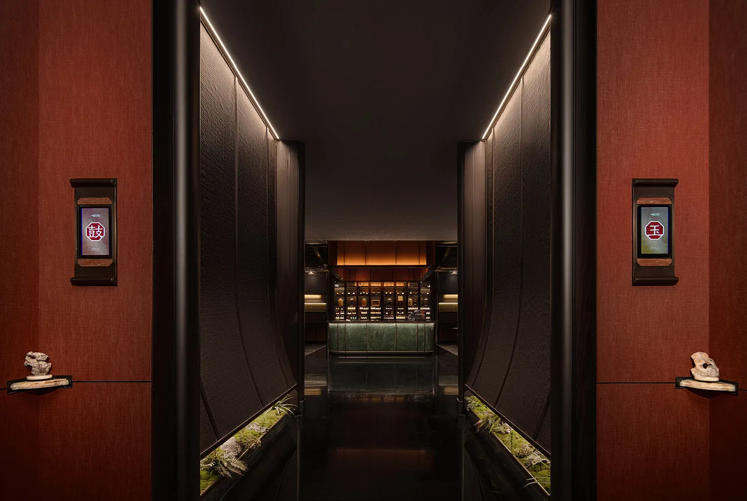 A hotel hallway with a dark carpet, potted plants, and scattered bottles, possibly leading to a bar or dining area