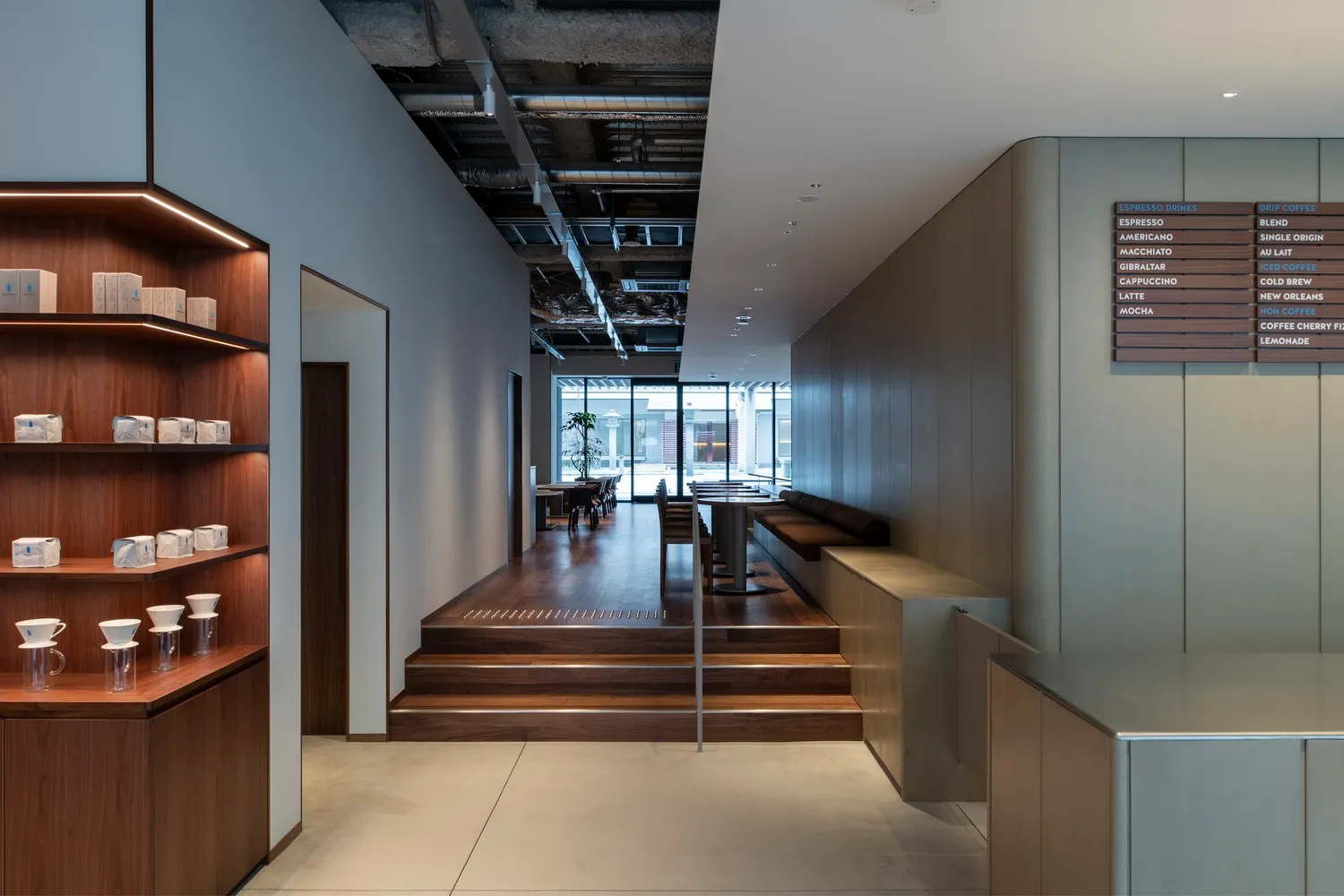 A modern lobby with wooden floors and walls, featuring chairs and a potted plant, with a well-designed atmosphere