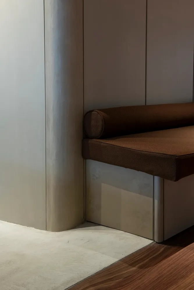 A modern and minimalist interior design featuring a wooden bench and metal accents against a silver wall, with natural light pouring in from a large window
