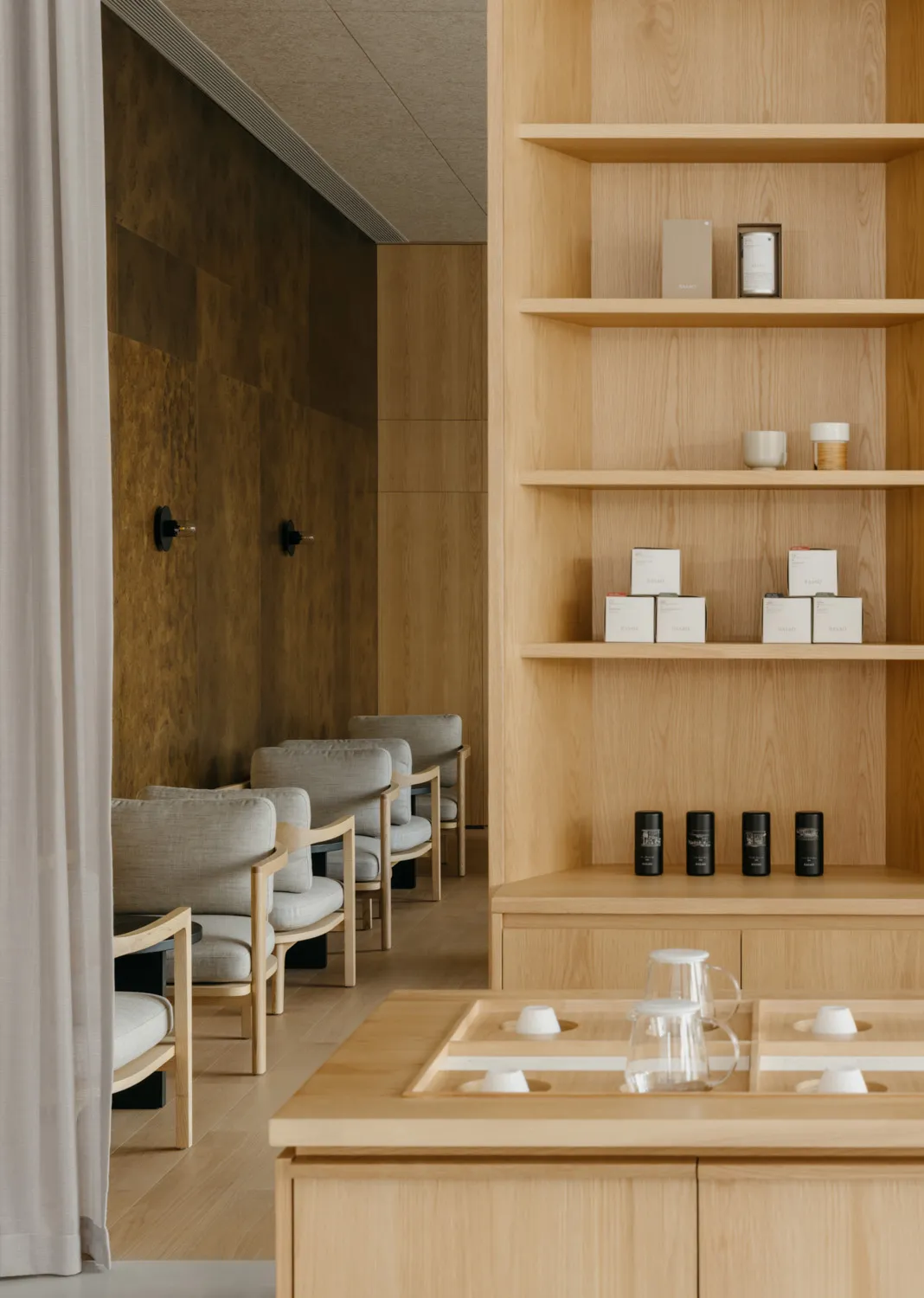 A modern interior design showroom with wooden walls and floors, featuring two couches, three chairs, and decorative bottles, creating a clean and inviting atmosphere