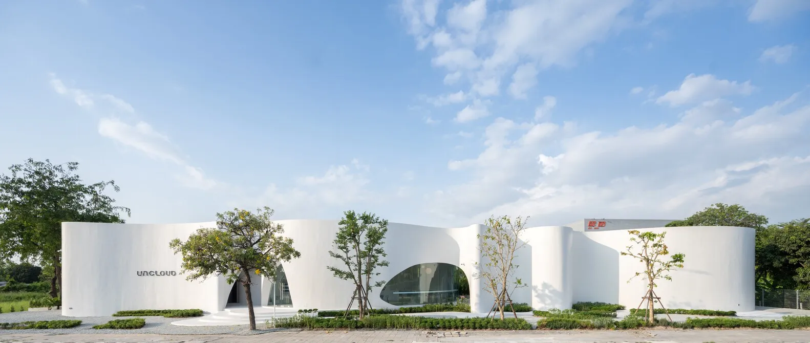 A modern building with a concrete exterior, multiple windows, and a curved design, surrounded by trees in an urban environment