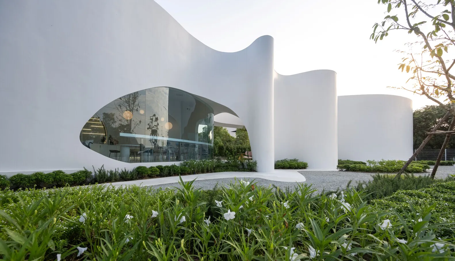 Contemporary museum space with a curved design, a large glass wall, and natural light, featuring chairs and a sophisticated atmosphere