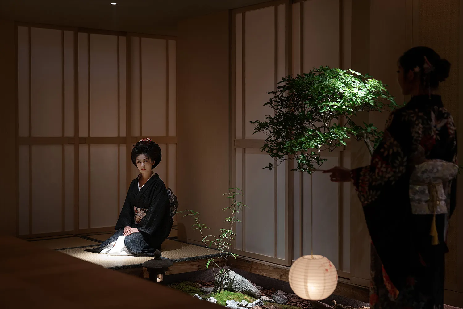 一位亞洲女性坐在地面上的寧靜沉思場景，房間光線昏暗，擁有木質牆壁與地板，並有一株小盆栽