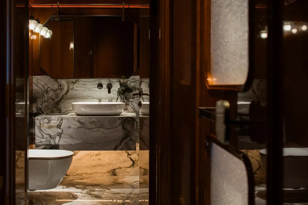 Bathroom with two sinks on a marble countertop, a wooden door, and a bowl near one sink, in a clean and organized space