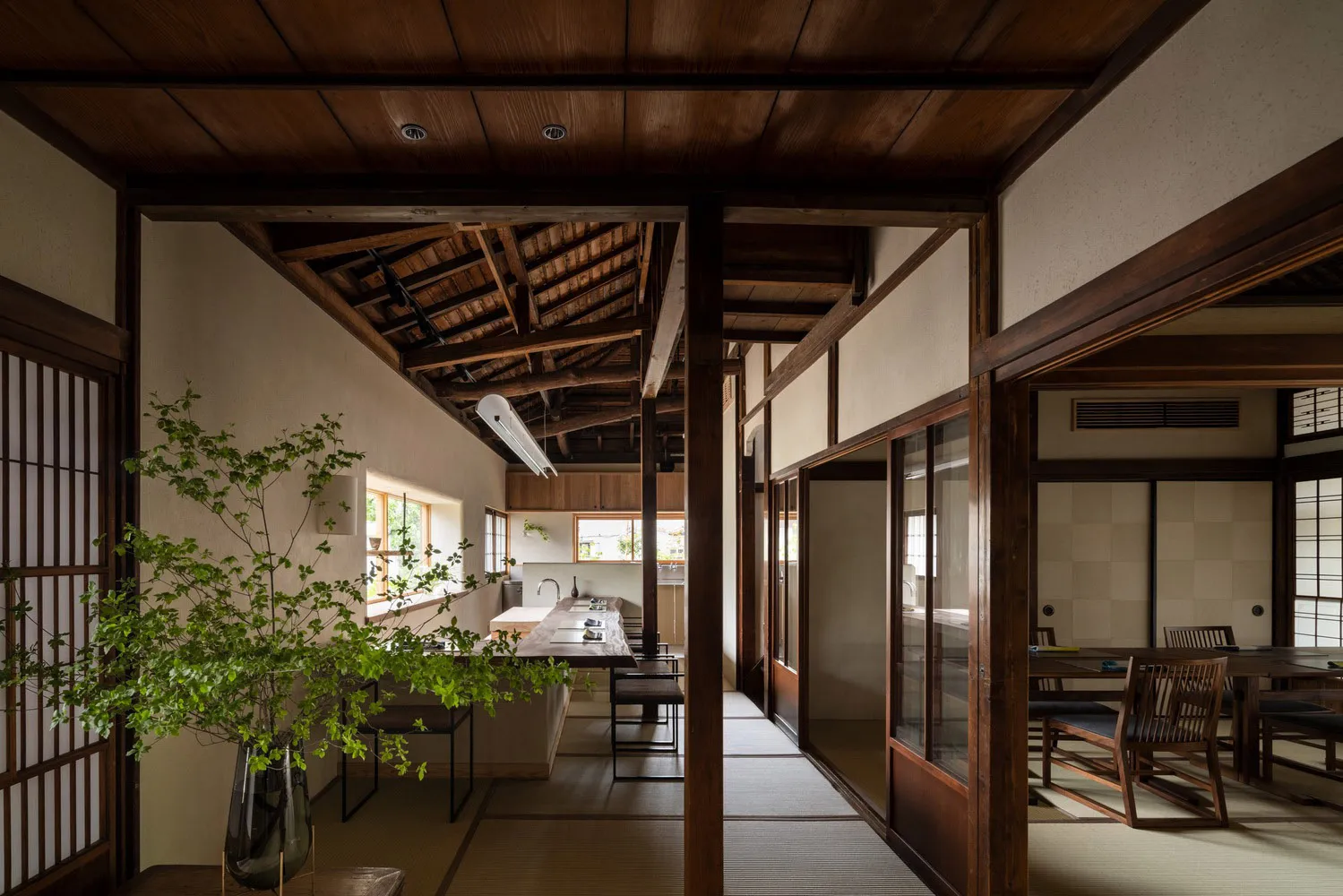 A well-lit, inviting space with wooden floors and walls, featuring a dining area, kitchen, and living room with a couch and potted plants
