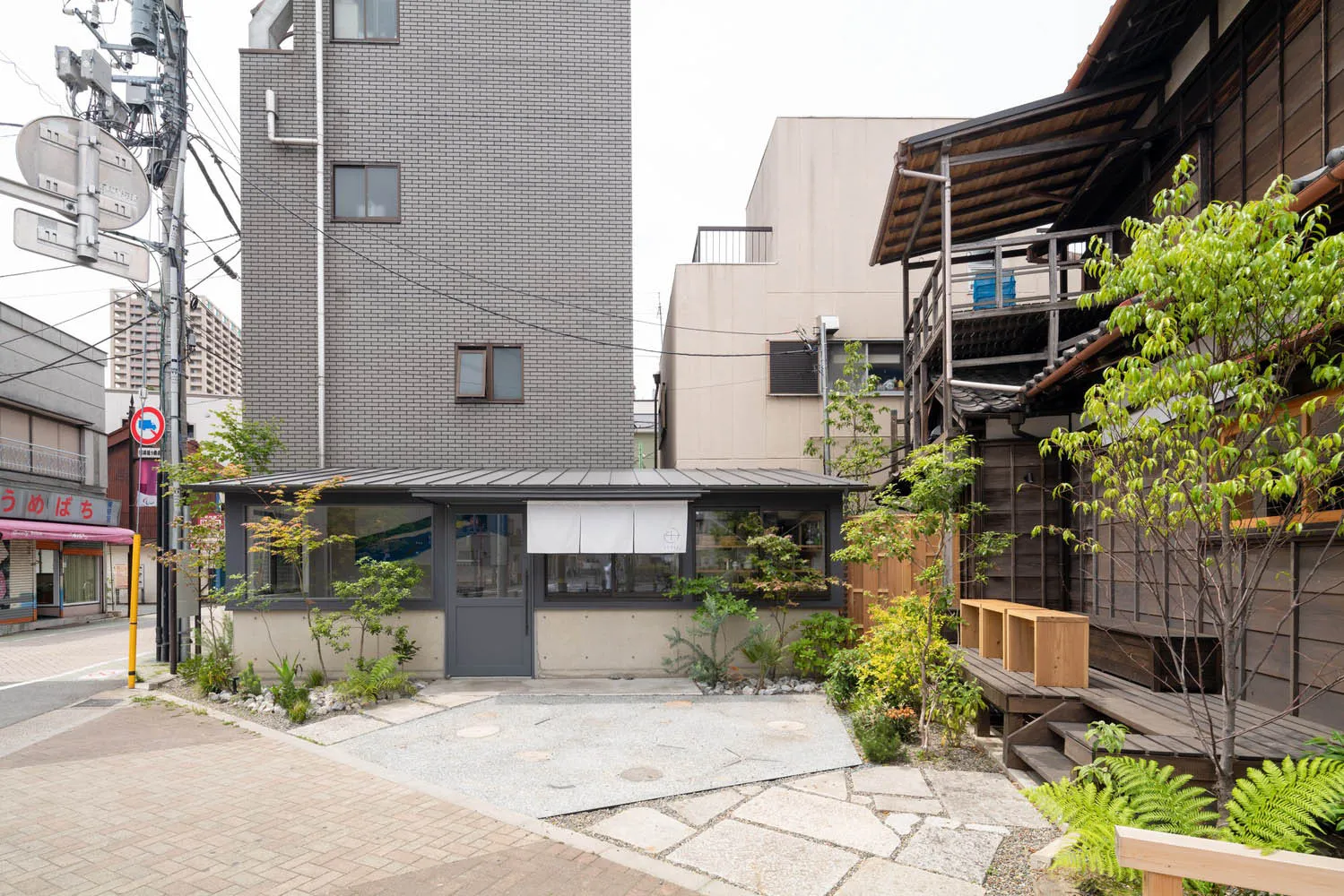 A city scene with a brick building and a modern building next to each other, featuring balconies and potted plants