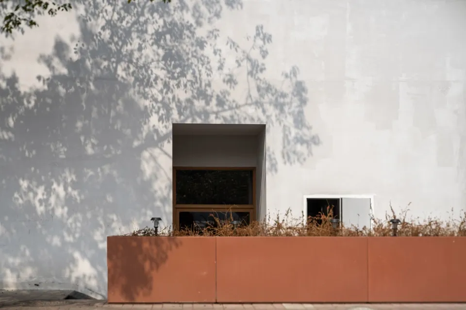 A traditional house with a red brick wall and two windows, one larger than the other, with a textured brick appearance and natural daylight
