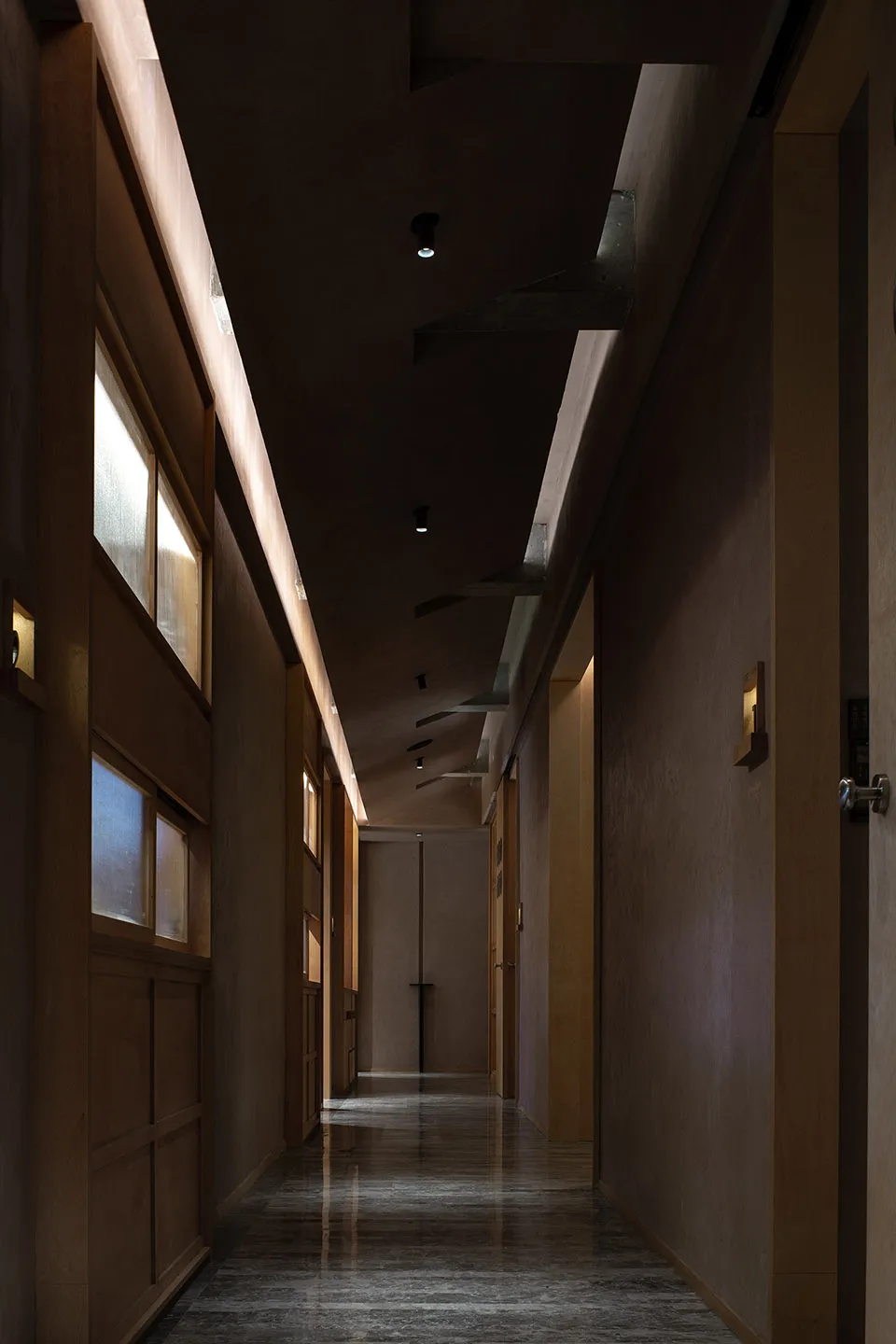 Dimly lit hallway with wooden doors, wooden walls, and natural light from two windows