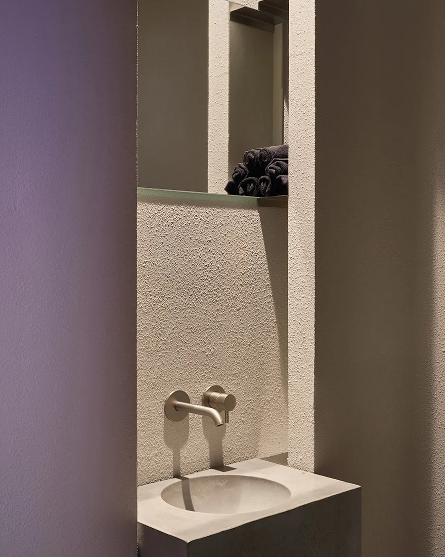 Modern bathroom with a wall-mounted sink, two faucets, and towels hanging nearby