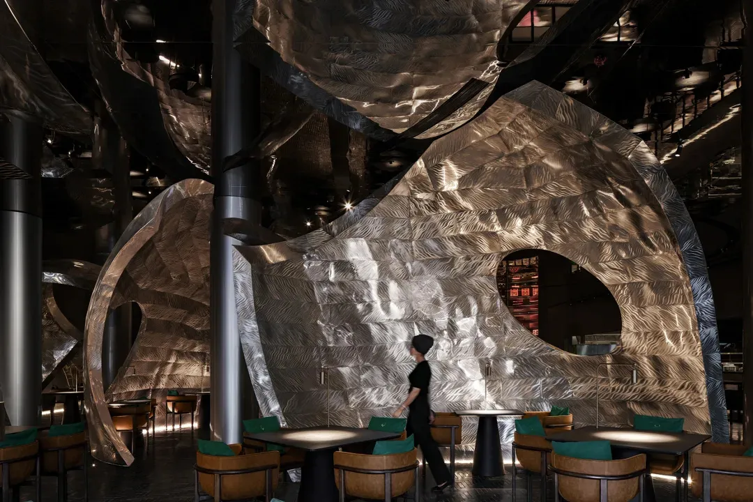 Modern restaurant interior with tables, chairs, and a bar, featuring metallic elements and a contemporary design