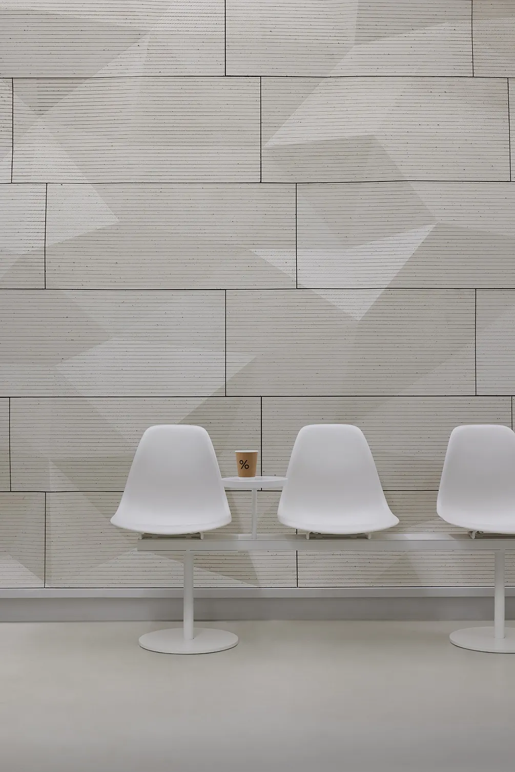Modern dining area with two white chairs and a small table in front of a wall with a unique brick pattern design