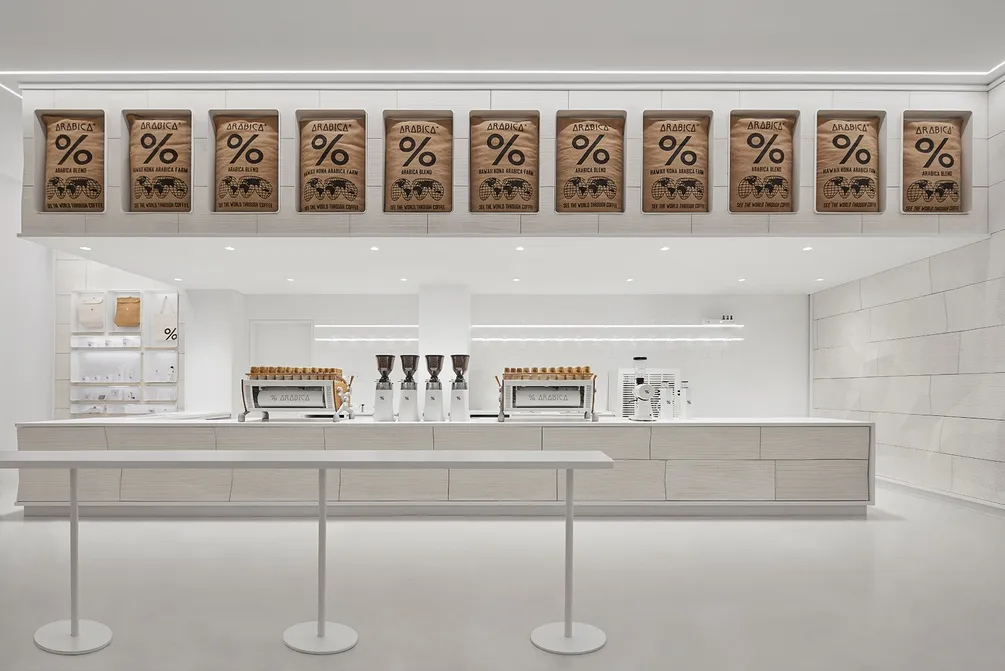 Industrial kitchen with white walls and floors, featuring coffee machines and cups, with a focus on functionality and efficiency
