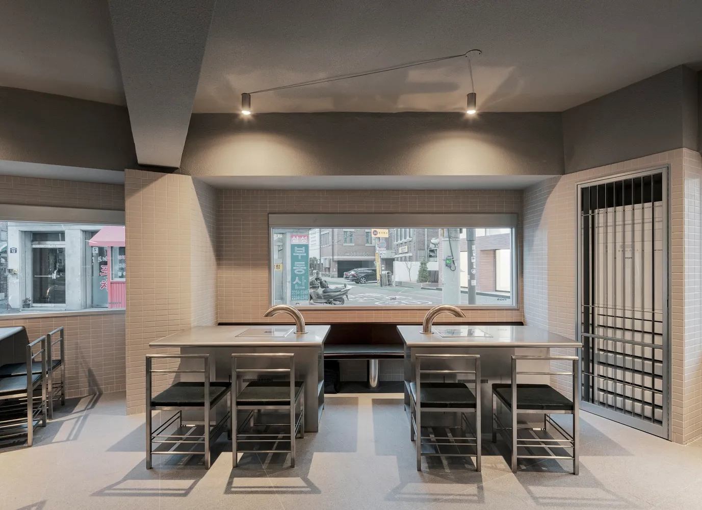 Empty restaurant dining area with two tables and chairs, a kitchen with sink and refrigerator, clean and well-organized space