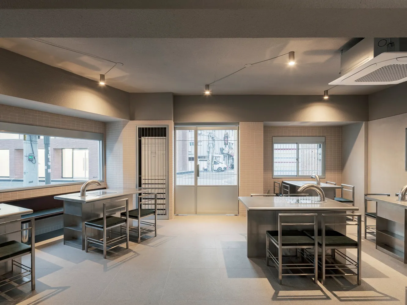 An empty kitchen with white walls and floors, featuring two dining tables, several chairs, and three sinks, appearing clean and well-organized