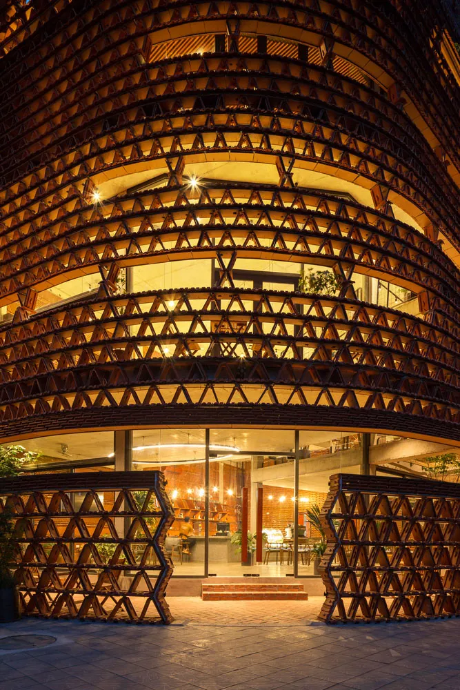 一座現代建築，前方有大型木構，設有室內外椅凳與盆栽的座位區