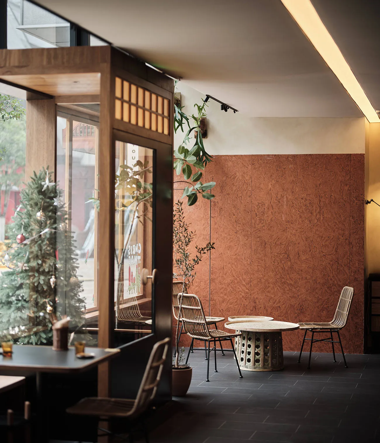 Modern restaurant interior with a dining area, bar counter, and potted plants, featuring red brick walls and a warm atmosphere