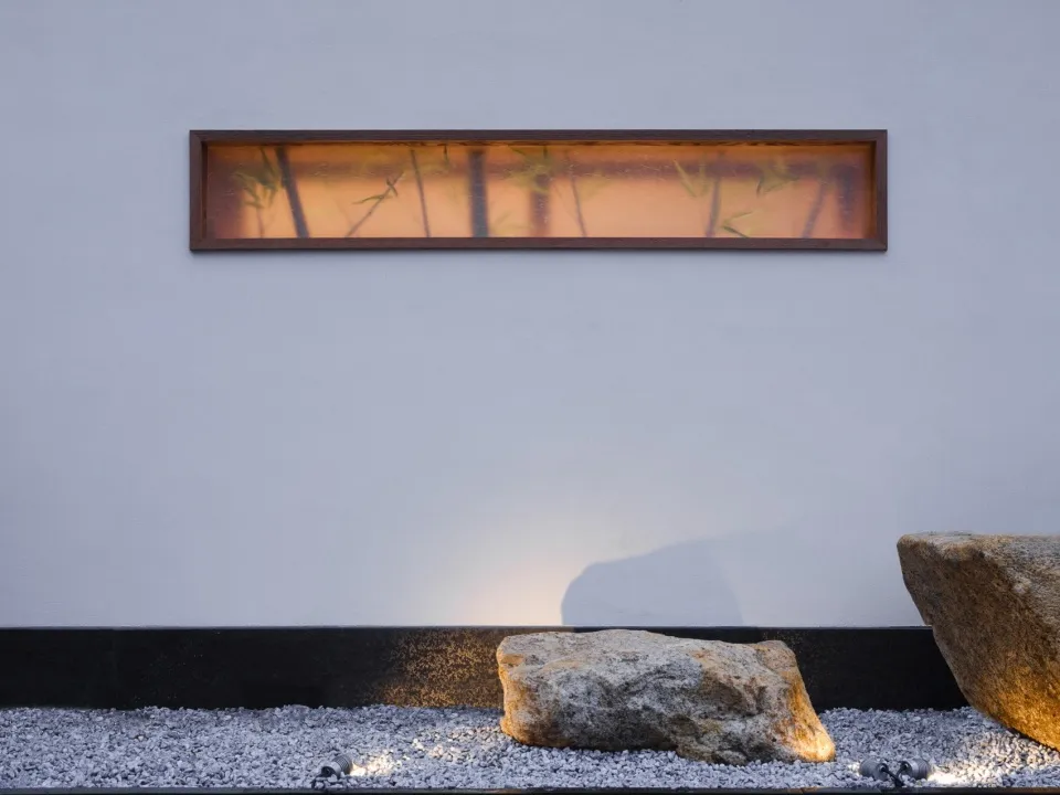 A modern space with a rock wall featuring a window and two rocks, a bench, and a bright atmosphere