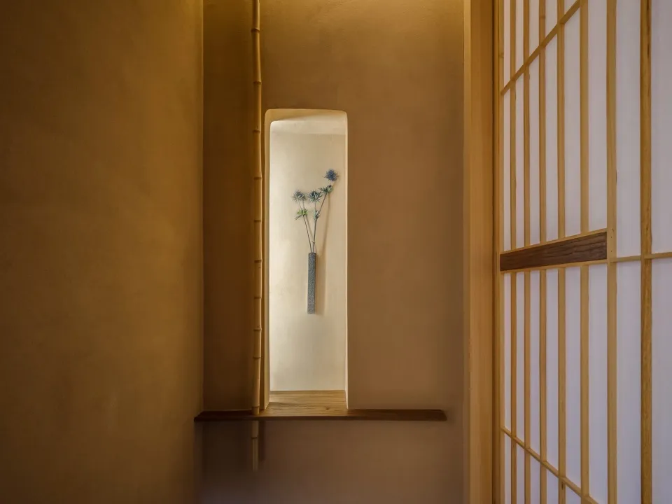 A calm and serene hallway with a concrete wall, two vases with flowers, and a minimalist aesthetic