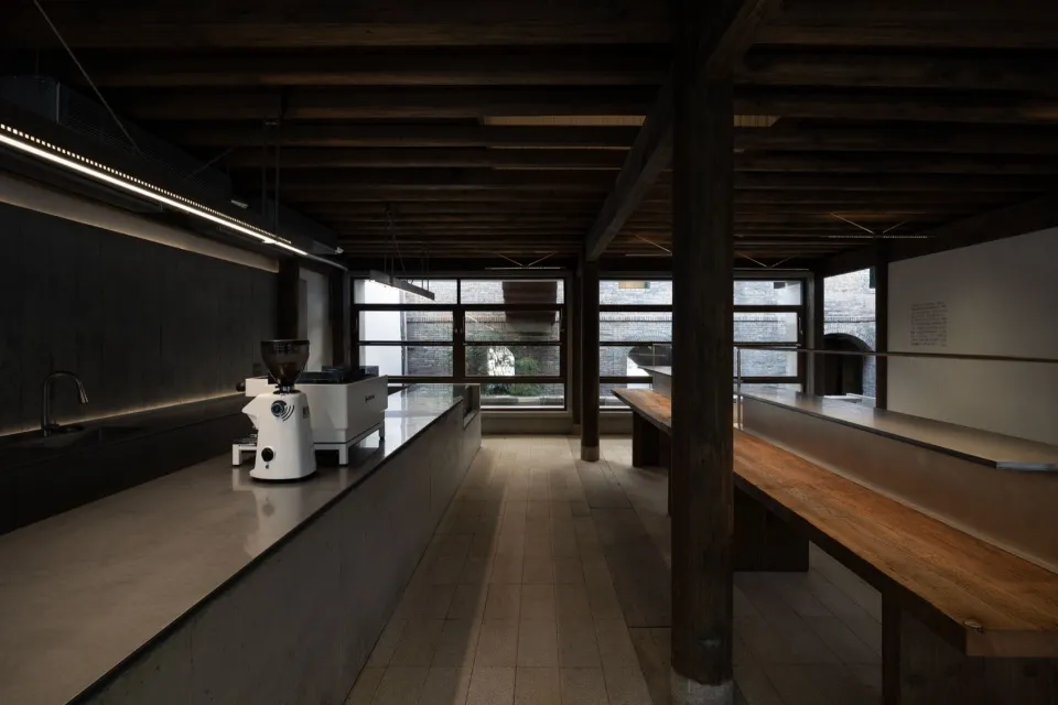 Rustic industrial kitchen with a wooden dining table, chairs, coffee makers, sink, and refrigerator