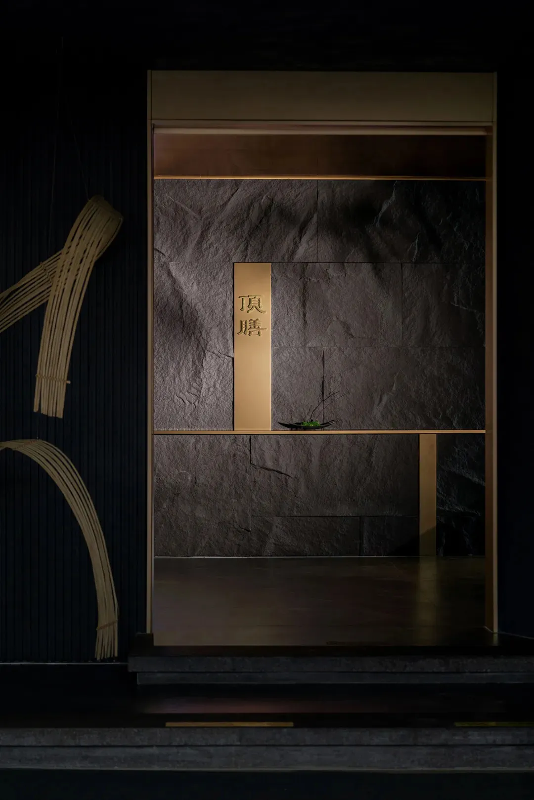 A serene Asian-style interior space with a stone wall, wooden countertop, and two doors, featuring a mix of stone and wood elements