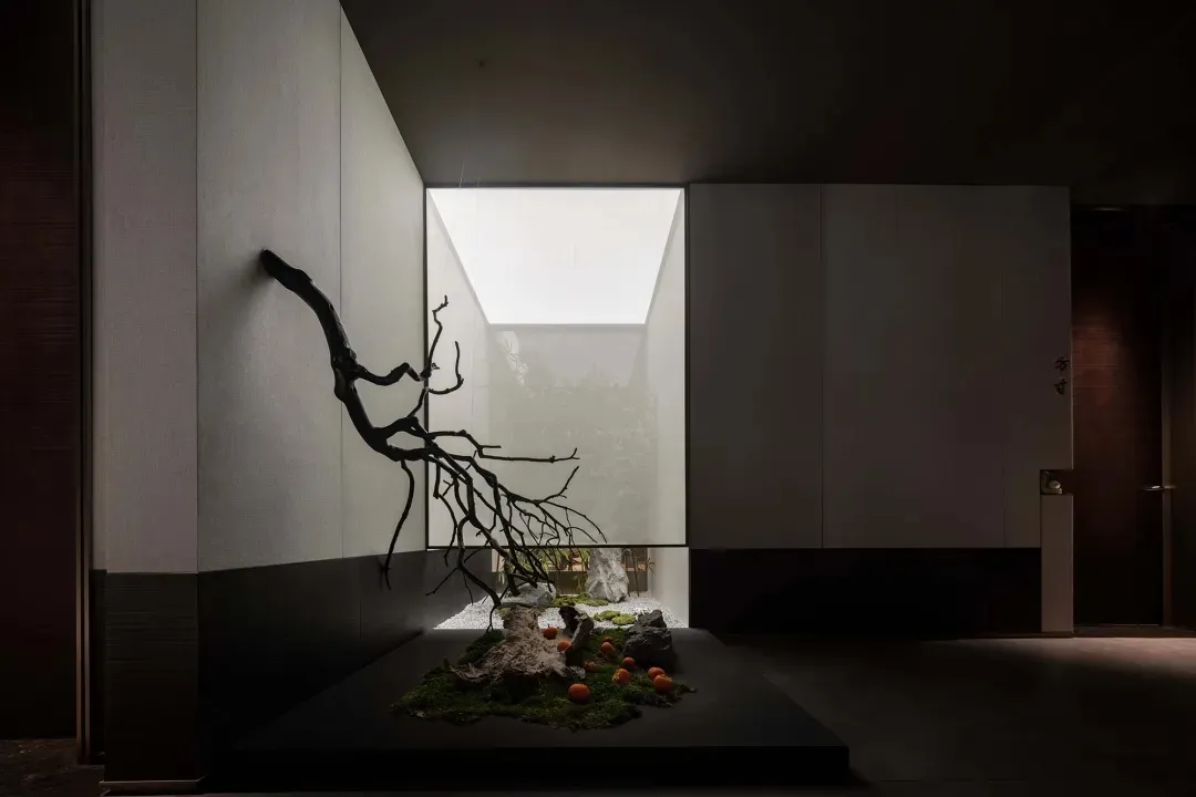 A living area with a tree sculpture made of branches and rocks as its centerpiece, blending nature and modern design elements