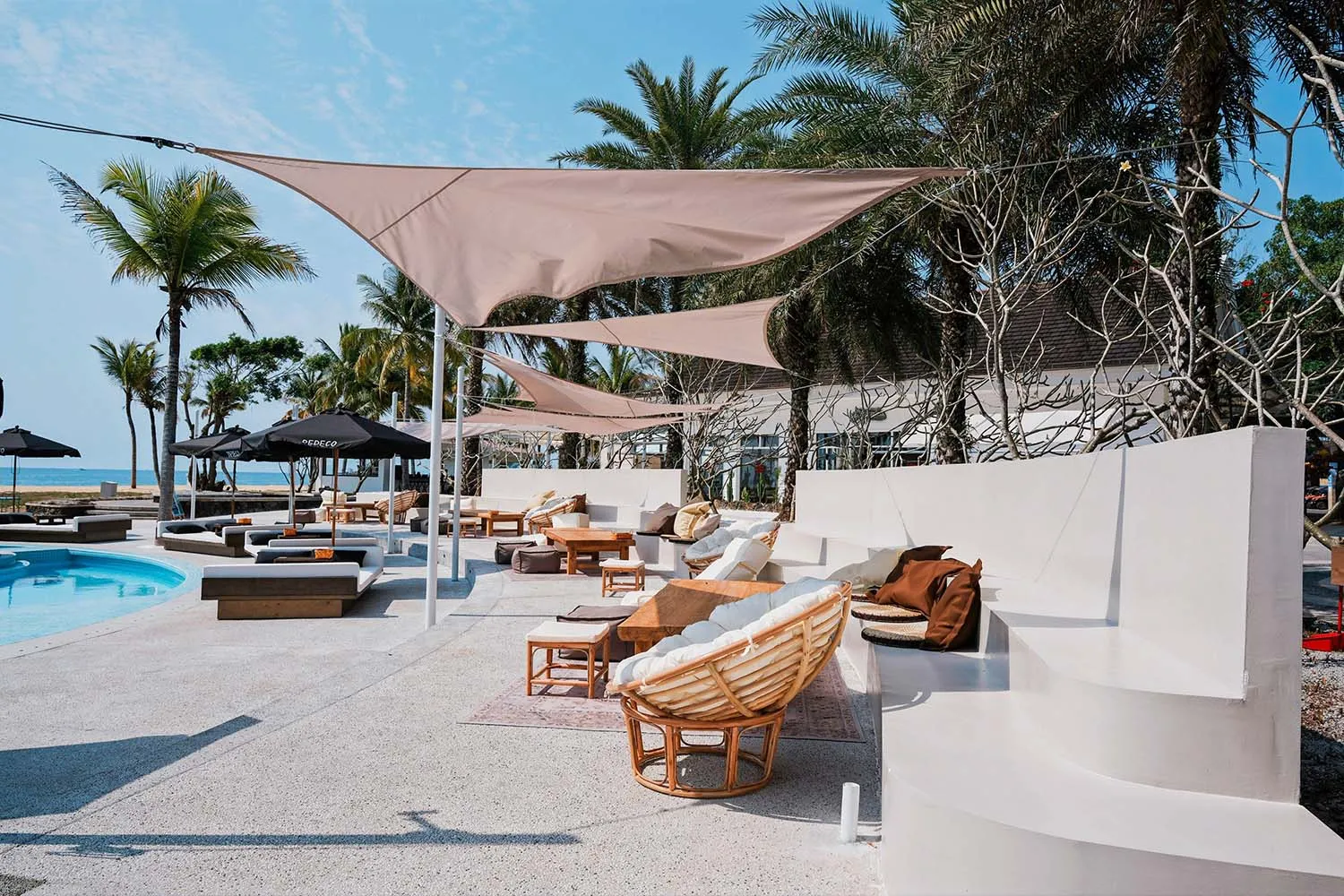 A resort patio with multiple chairs and couches under large umbrellas, creating a shaded and inviting seating area