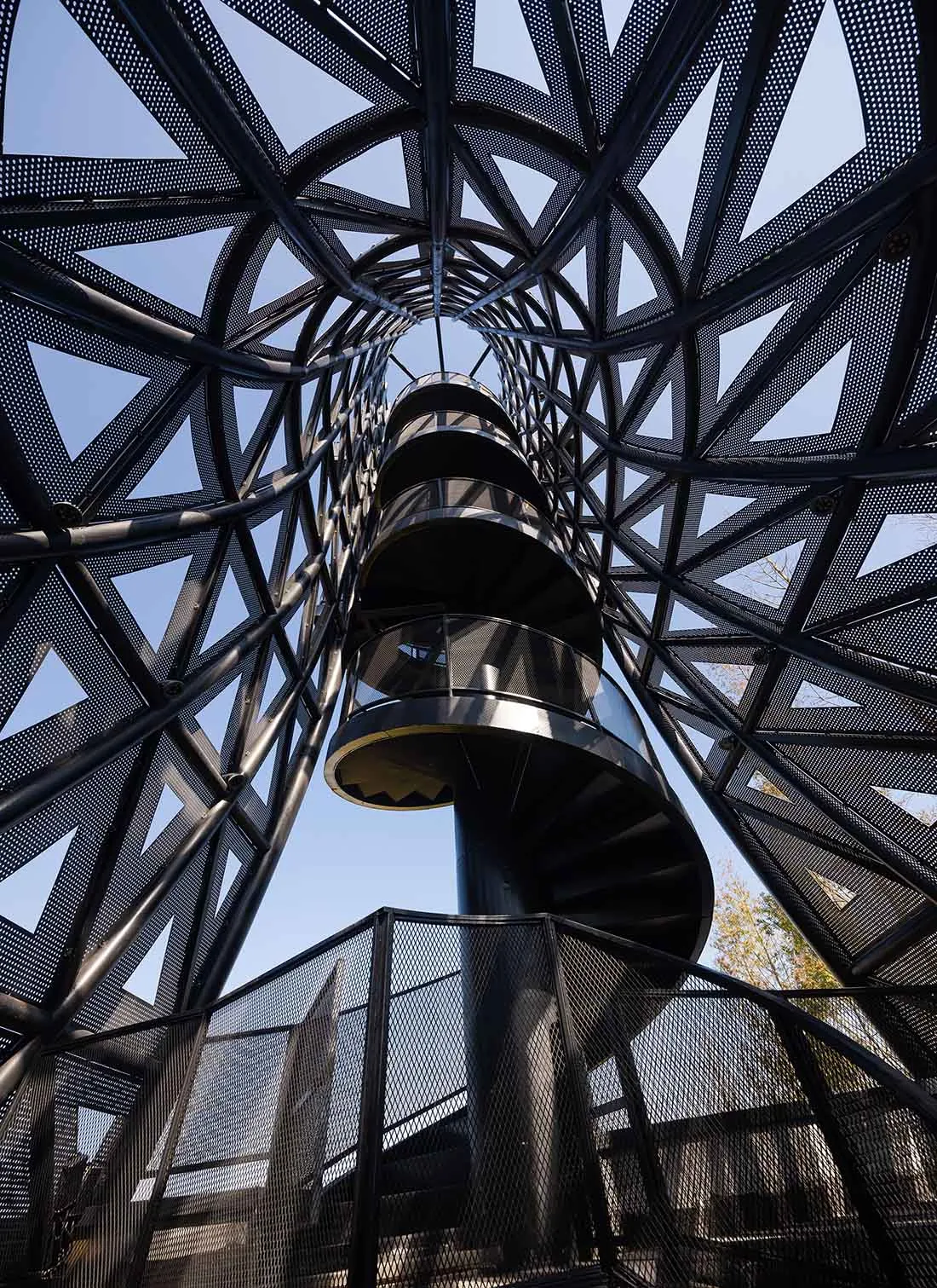 A rendered image of a spiral staircase with a black metal railing and surrounding structure, set against a blank background