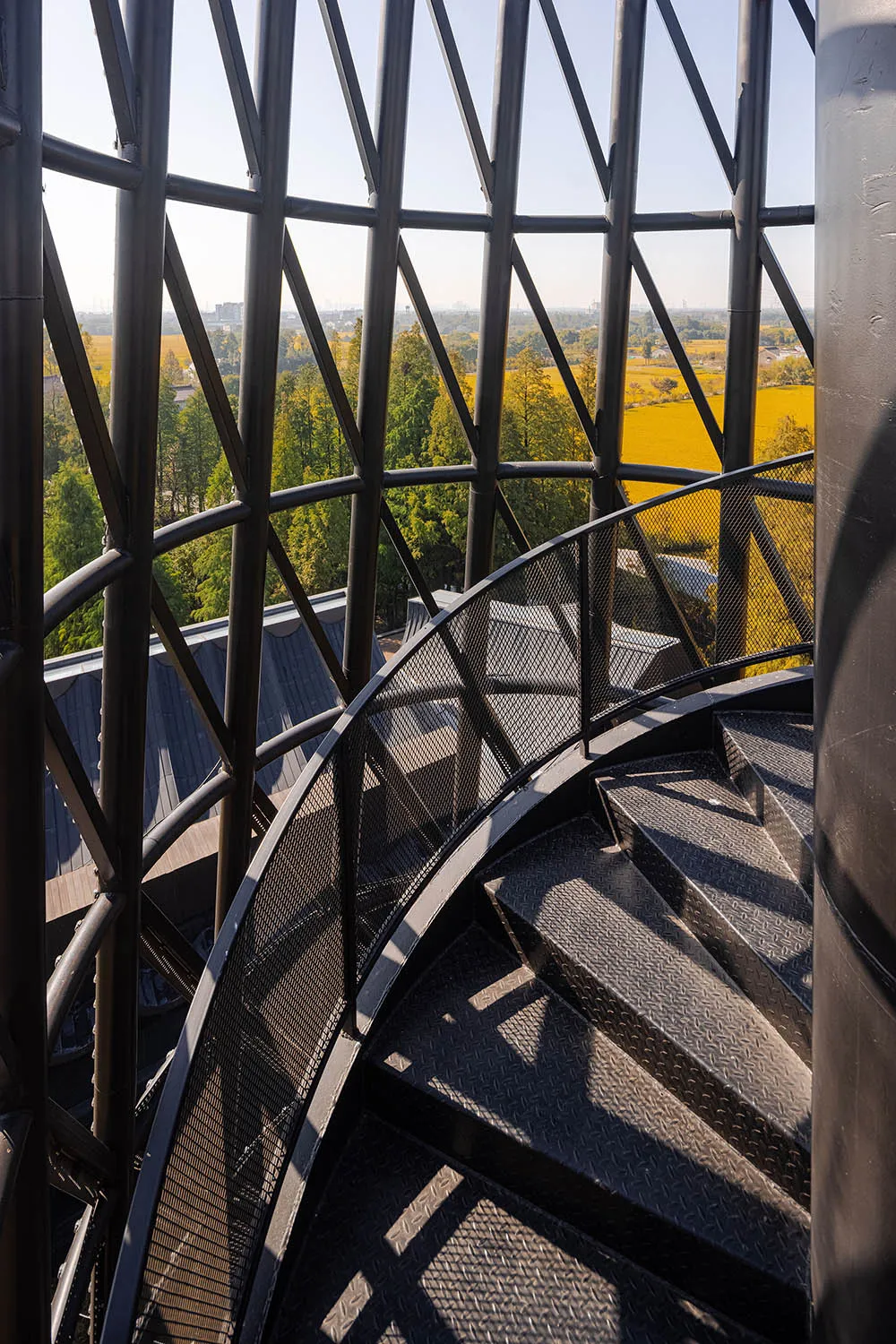 A rendered image of a spiral staircase with a metal railing surrounded by trees, creating a sense of openness and connection to nature