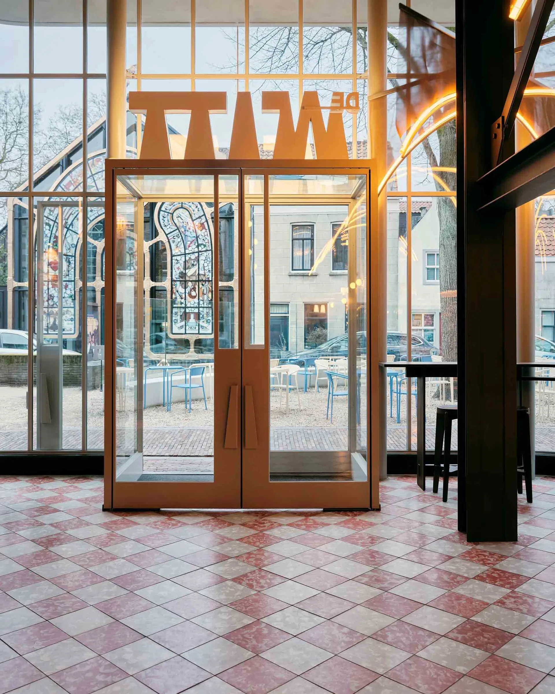 A welcoming entrance with a glass door, multiple chairs, and dining tables, set in a well-lit space