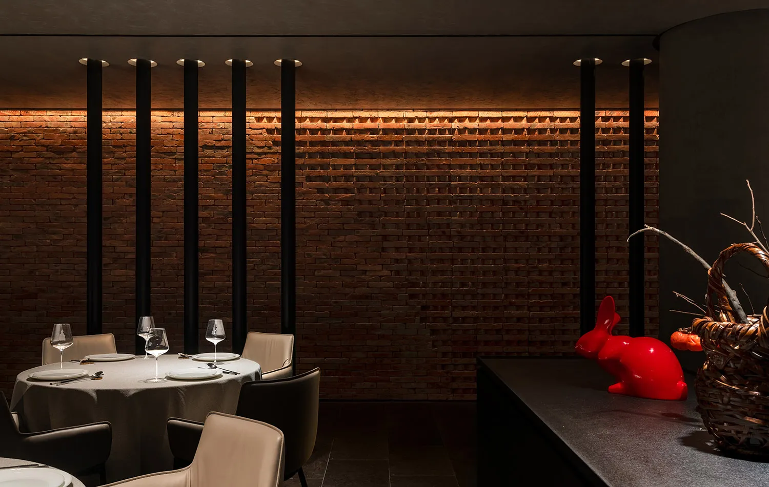 Dimly lit restaurant interior with brick walls, stone floor, and chairs with wine glasses