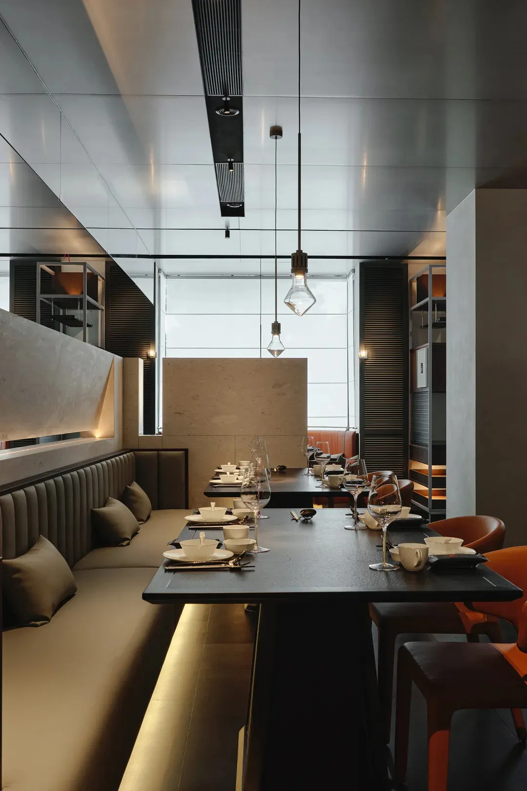 A dimly lit restaurant interior with modern furniture and table settings, featuring wine glasses, cups, and vases, creating a sophisticated atmosphere