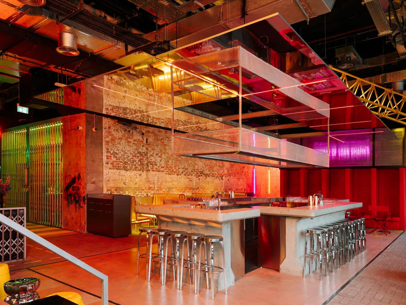 Industrial kitchen with a modern design, featuring a large island, stools, chairs, and a red-painted wall, with a warm atmosphere created by red lighting