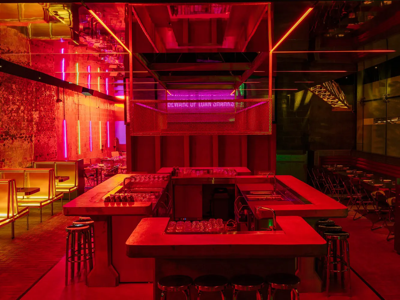 A lively bar area with a long red counter and stools, surrounded by chairs in a warm and inviting atmosphere
