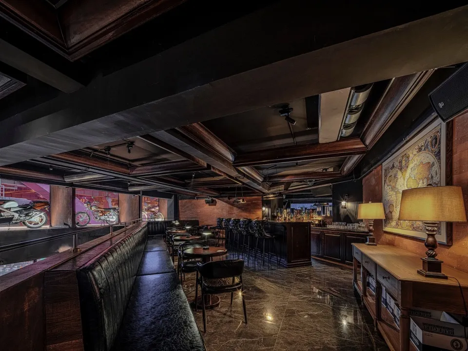 Modern bar area with a wooden wall, a long bar counter, dining tables, and comfortable seating for patrons