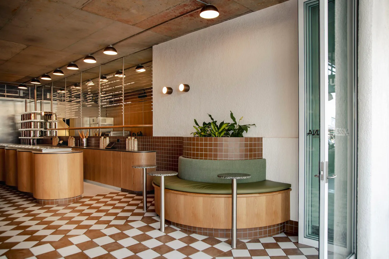 A cozy cafe with a round table surrounded by chairs, potted plants, and modern tiled walls